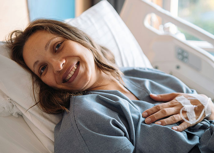 Smiling patient in hospital bed with IV line, illustrating wild and funny post-anesthesia acts caught by doctors and nurses.