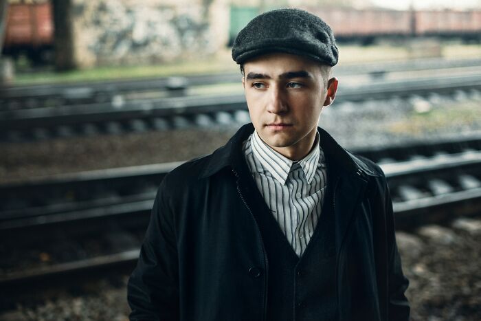Young man wearing a cap and dark coat, standing near train tracks, representing incredible minds and genius without degrees.