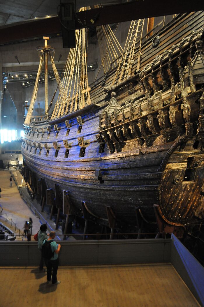 Massive old wooden ship exhibited indoors towering over visitors, evoking megalophobia with its immense size and detailed structure.