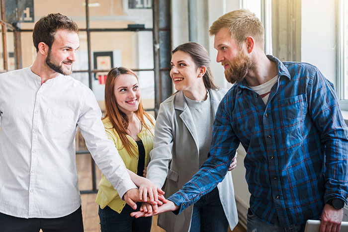 Group of coworkers joining hands in teamwork gesture, illustrating subtle red flags that mean job insecurity. Group of coworkers joining hands in teamwork gesture, illustrating subtle red flags that mean job insecurity.