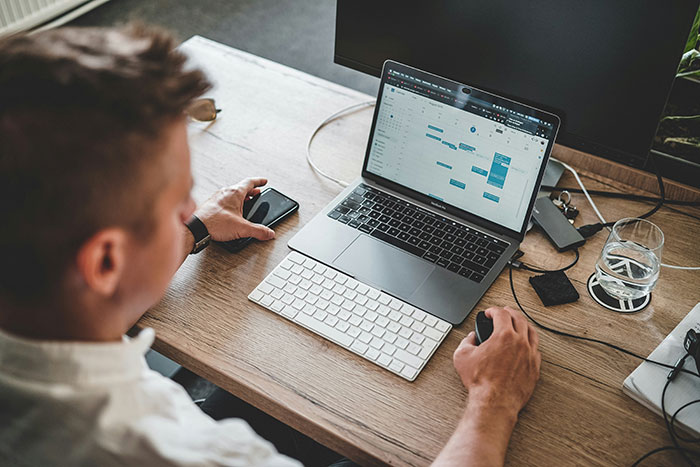 Man working on laptop and phone at desk, highlighting subtle red flags that indicate job insecurity risks.