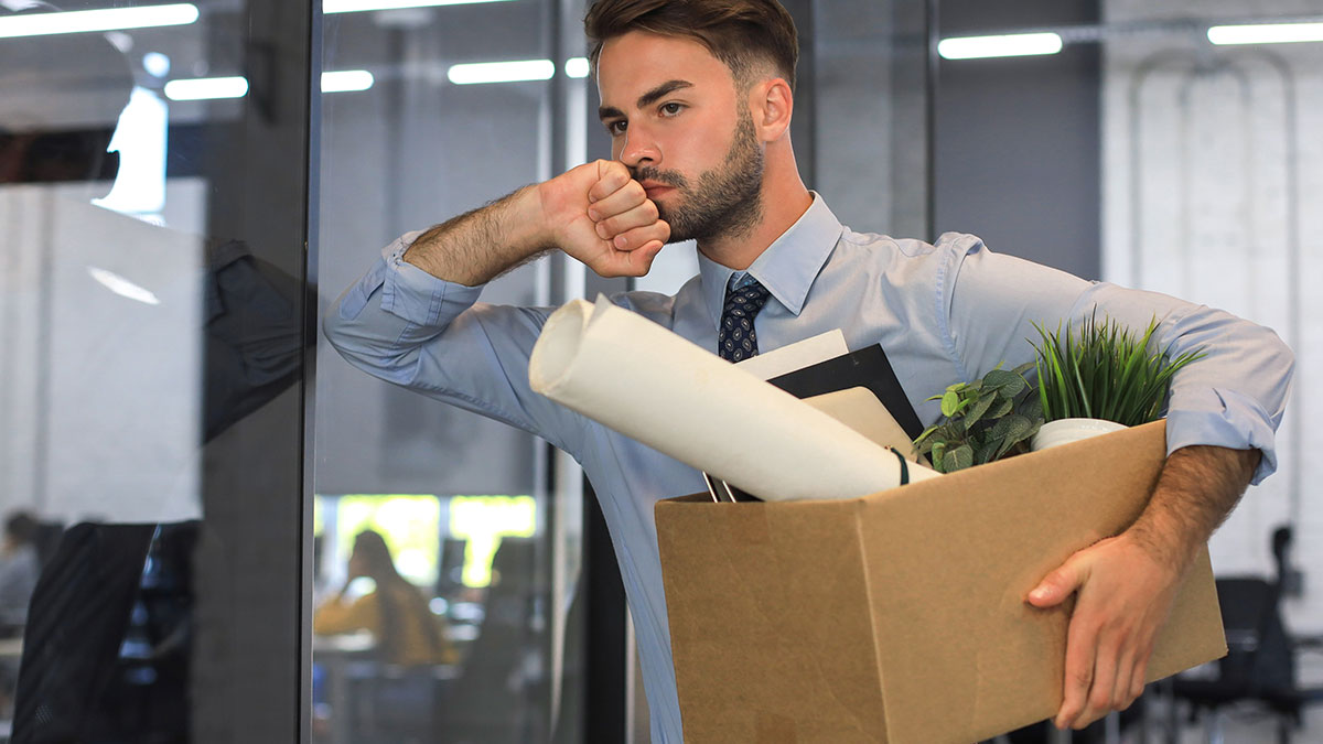Young man packing belongings in a box showing subtle red flags of job insecurity in a modern office environment