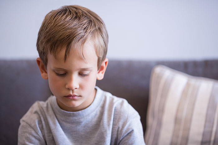 Young boy sitting indoors looking down with a neutral expression, illustrating a little spoiled son and family gift conflict.
