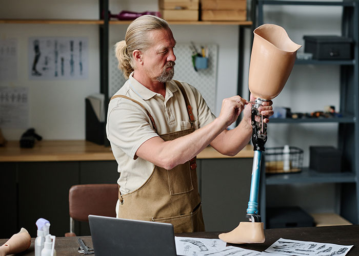 Man examining a prosthetic leg in a workshop, illustrating a man demands cousin pay for his cruel prank scenario. Man examining a prosthetic leg in a workshop, illustrating a man demands cousin pay for his cruel prank scenario.