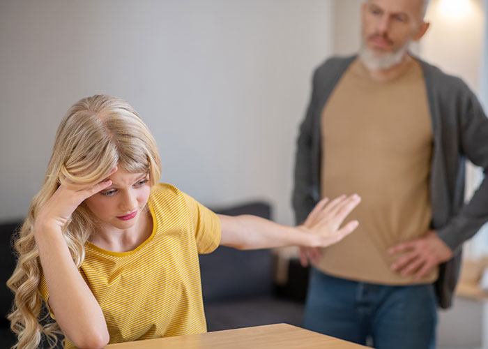 Young woman upset, refusing to talk, while man demands payment for cruel prank in tense family dispute.