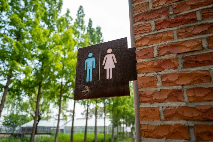 Restroom sign on brick wall outdoors, symbolizing the unseen side of a digital nomad’s life experience.