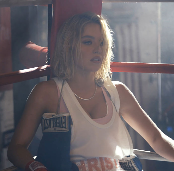 Sydney Sweeney wearing boxing gloves and sportswear, posing inside a boxing ring with moody lighting. Sydney Sweeney wearing boxing gloves and sportswear, posing inside a boxing ring with moody lighting.