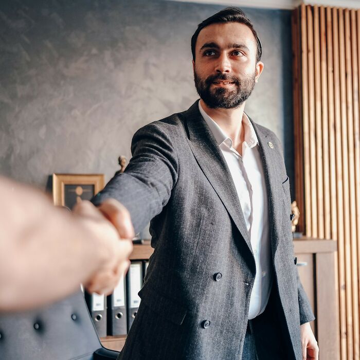 Man in gray suit shaking hands in an office, representing professional interactions and workplace scandals.