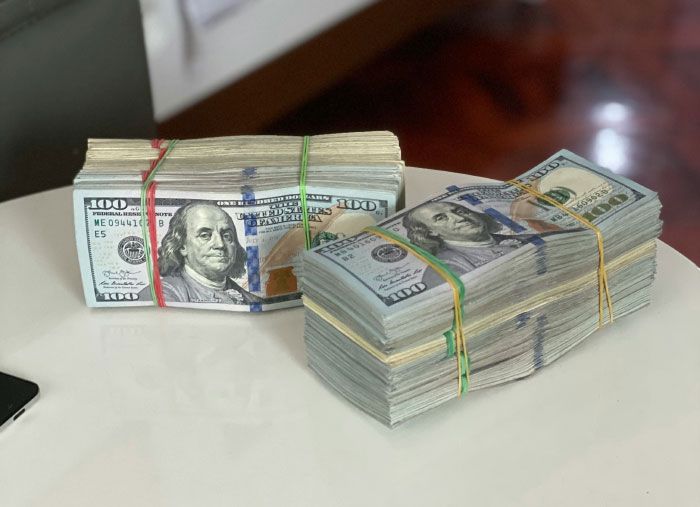 Stacks of US hundred-dollar bills bound with rubber bands on a white table representing AI industry dirty secrets.