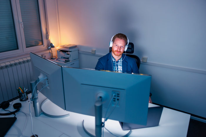 Man wearing headphones working on multiple monitors in an office, related to AI industry insights and technology secrets.