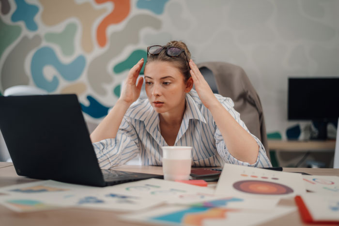 Woman working on a laptop with charts and papers nearby, appearing stressed, relating to AI industry dirty secrets.