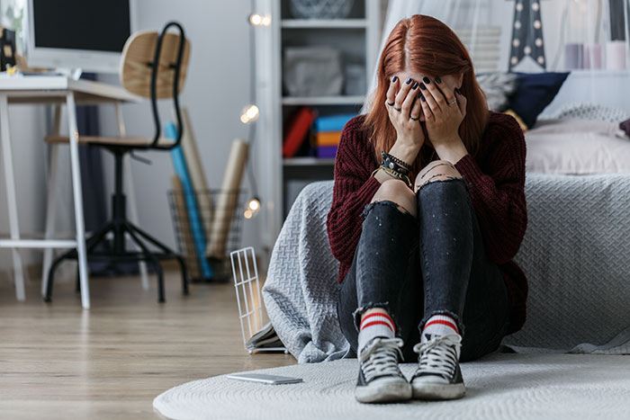 Teen girl sitting on floor in bedroom, upset and covering her face, depicting insecurity about stepmother dynamics. Teen girl sitting on floor in bedroom, upset and covering her face, depicting insecurity about stepmother dynamics.