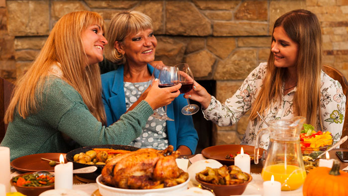Three women clinking wine glasses at Thanksgiving dinner, with a feast including turkey and candles on the table. Three women clinking wine glasses at Thanksgiving dinner, with a feast including turkey and candles on the table.