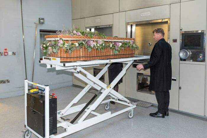 Man in black coat standing by a coffin on a lift in a funeral home, illustrating unexpected funeral moments.