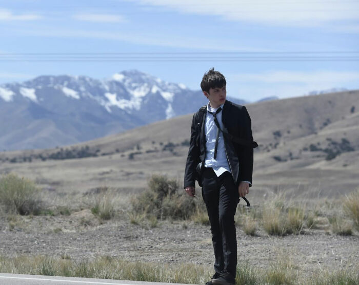 Young man in a disheveled suit walking alone on a roadside with mountains in the background, evoking a chaotic hotel room scene. Young man in a disheveled suit walking alone on a roadside with mountains in the background, evoking a chaotic hotel room scene.