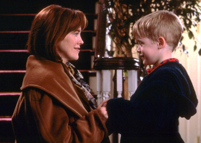 Scene from Home Alone movie showing a woman and young boy holding hands in a warmly lit home setting.