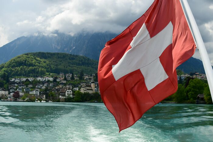 Swiss flag waving on a boat with a scenic lakeside town and forested mountains, highlighting historical facts unknown until recently