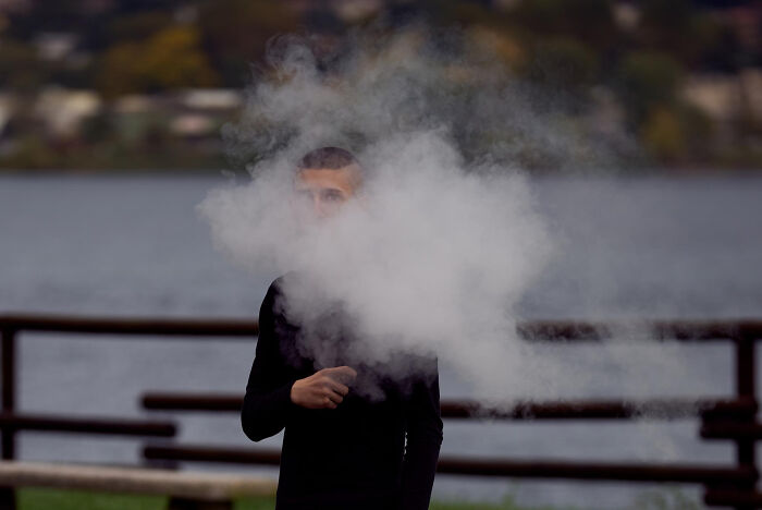 Person surrounded by thick smoke outdoors near a lake, illustrating overrated and overpriced experiences concept.