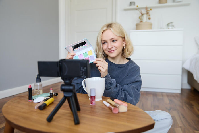 Young woman recording a video review using makeup products, sharing her thoughts on overrated and overpriced experiences.