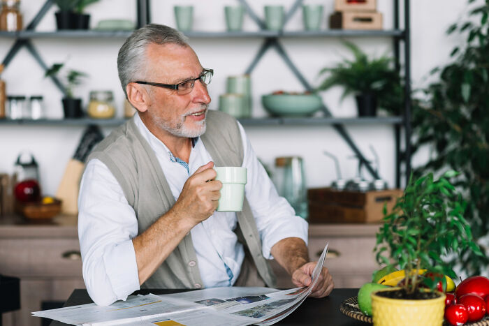 Older man enjoying coffee and reading a newspaper in a cozy kitchen, reflecting on overrated experiences.