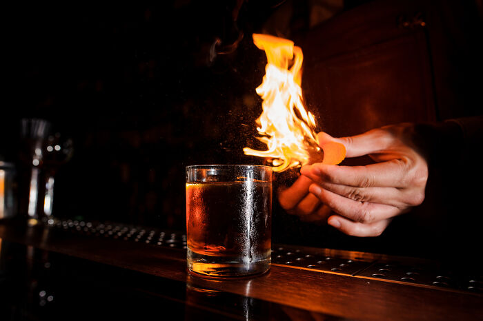 Bartender lighting a cocktail on fire at a dimly lit bar showcasing one of the overrated must-try experiences.