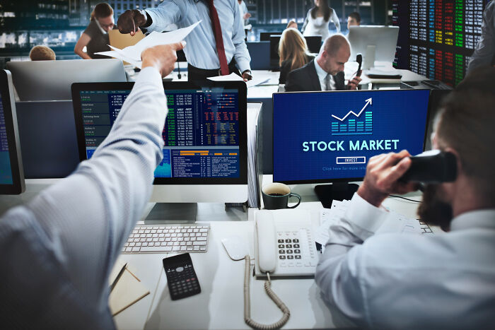 Traders busy at computers in a stock market office environment with multiple screens showing financial data.