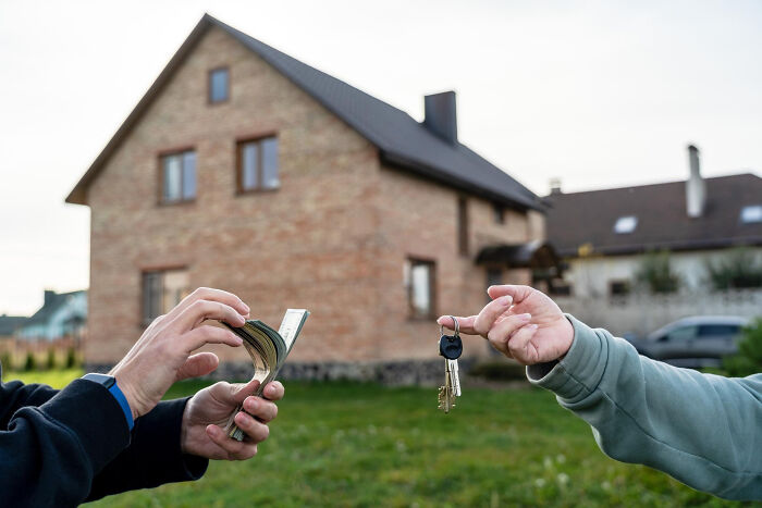 Hands exchanging house keys and cash outside a suburban home illustrating overrated and overpriced experiences.