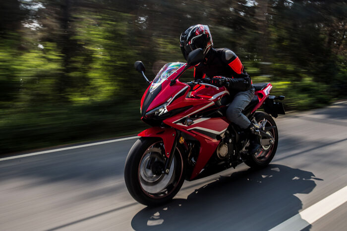Person riding a red sport motorcycle on a forest road, illustrating experiences that may be overrated or overpriced.