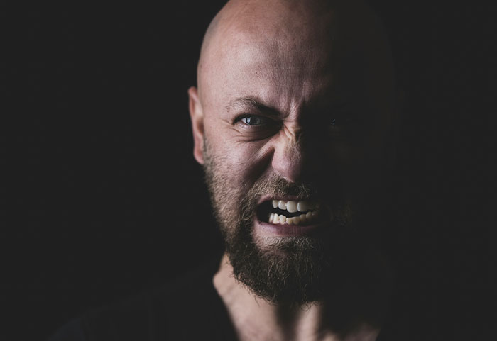 Angry bearded man showing intense emotions in a dark setting, reflecting the impact of female roasts on men.
