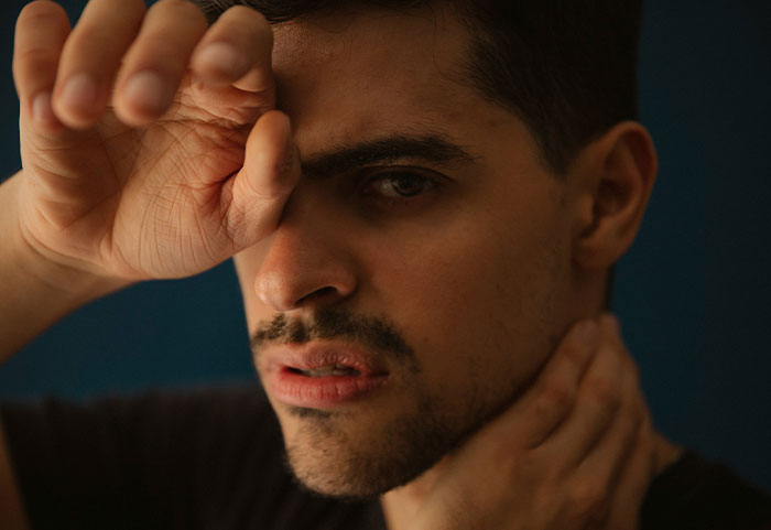 Close-up of a man with a distressed expression, holding his face and neck, illustrating impact of female roasts.