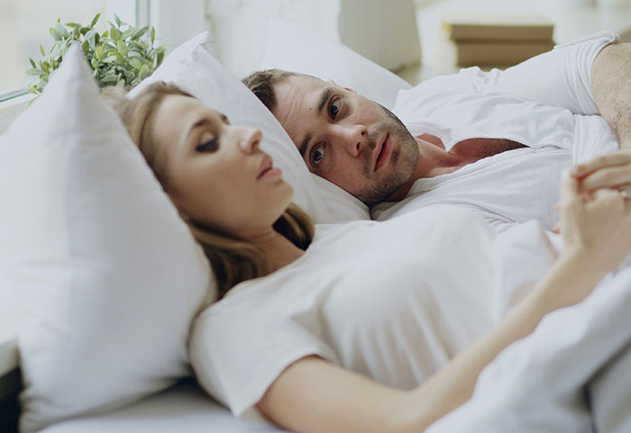 A woman giving a serious look while a man lies beside her, reflecting on female roasts hitting men hard.