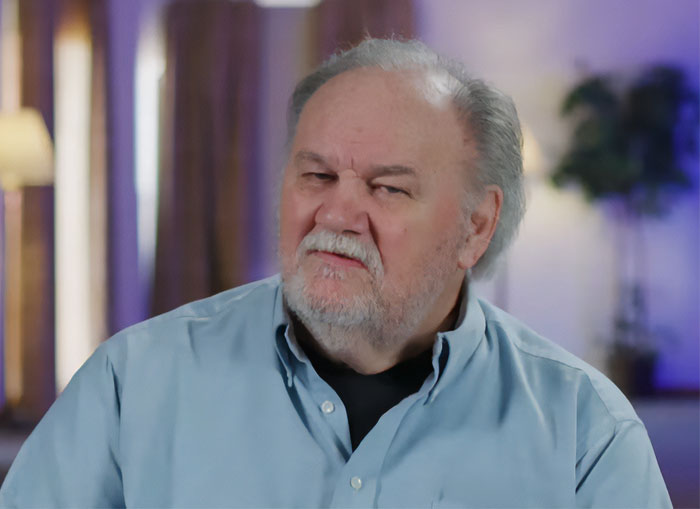 Older man with white hair and beard wearing a blue shirt, sitting indoors, related to Meghan Markle estranged hospitalized father story. Older man with white hair and beard wearing a blue shirt, sitting indoors, related to Meghan Markle estranged hospitalized father story.