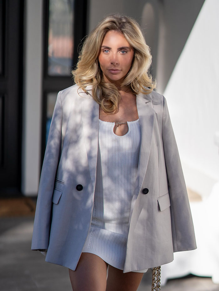 Blonde woman wearing a white dress and light gray blazer walking outdoors as snitch who reported Bonnie Blue to cops. Blonde woman wearing a white dress and light gray blazer walking outdoors as snitch who reported Bonnie Blue to cops.