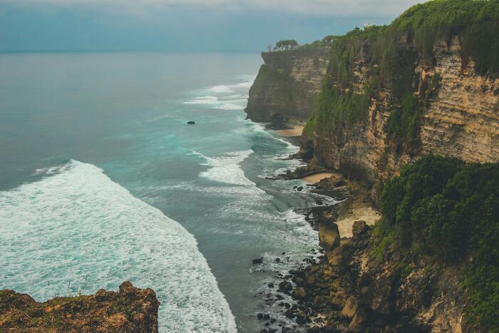 Ocean waves crashing against tall rocky cliffs covered with greenery, illustrating nature's powerful science facts.