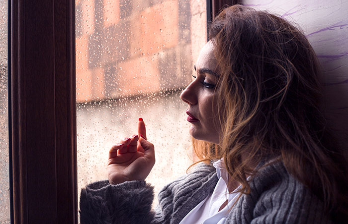 Woman in gray sweater staring sadly out a rainy window reflecting on couple’s first free Saturday turning sour. Woman in gray sweater staring sadly out a rainy window reflecting on couple’s first free Saturday turning sour.