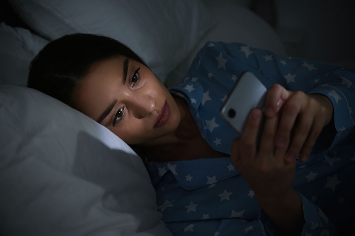 Woman in star-patterned pajamas lying in bed at night, looking upset while holding a smartphone. Woman in star-patterned pajamas lying in bed at night, looking upset while holding a smartphone.