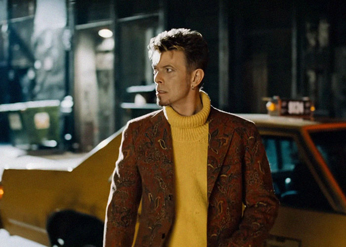 Person wearing a patterned jacket and yellow turtleneck standing near a parked car in an urban nighttime setting, interesting facts concept.