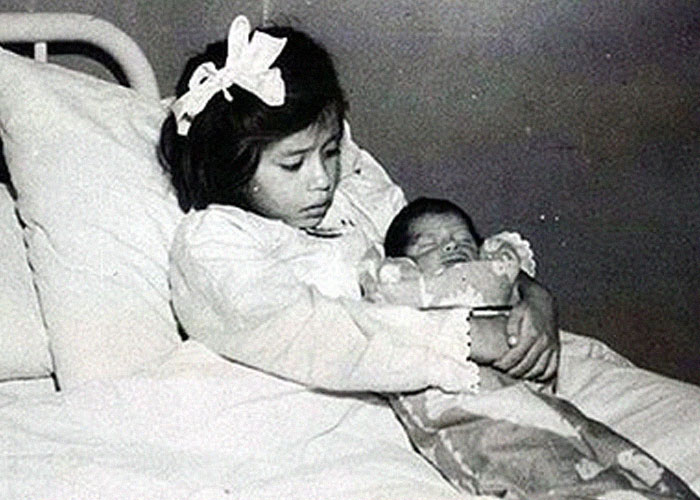 Vintage black and white photo of a girl holding a baby in bed, illustrating interesting Today I Learned facts.
