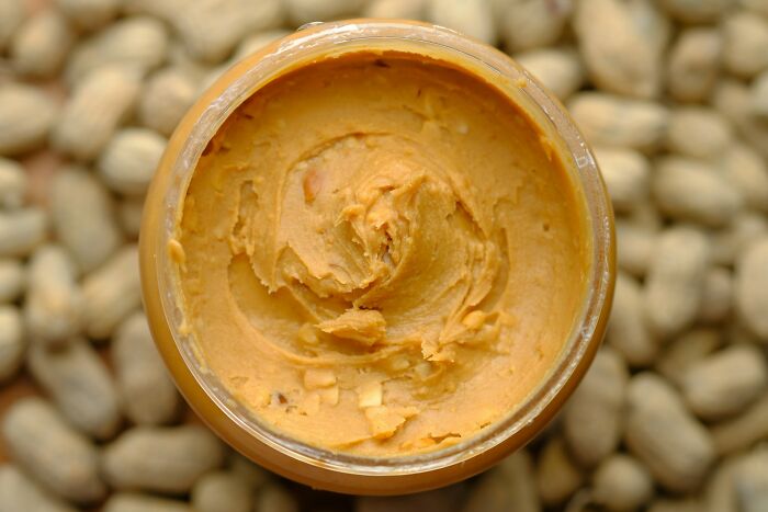 Close-up of creamy peanut butter in a jar with peanuts in the background illustrating unusual facts that sound made up but are true.