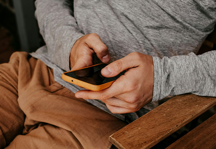 Person in casual gray sweatshirt holding smartphone, illustrating dad privileges discussed by 61 moms in parenting context.