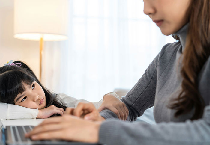 Mother working on a laptop while her daughter looks on, illustrating the emotion behind dad privileges and family dynamics.