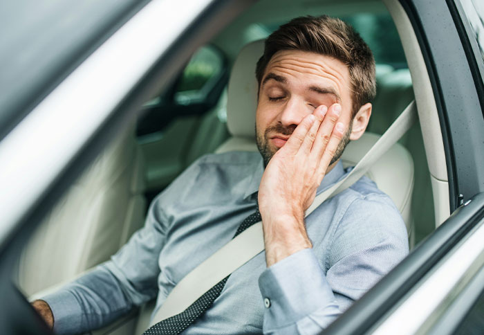 Tired man sitting in car rubbing his eyes illustrating dad privileges and parental exhaustion from moms' perspective.