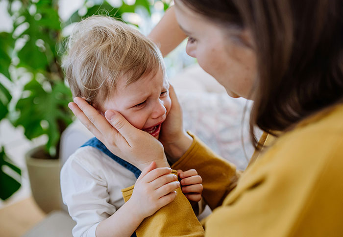 Mom comforting crying toddler in a home setting, illustrating challenges related to dad privileges and parenting struggles.