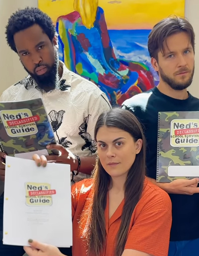 Three people holding Ned’s Declassified School Survival Guide manuals, one woman in orange in front, two men behind her. Three people holding Ned’s Declassified School Survival Guide manuals, one woman in orange in front, two men behind her.