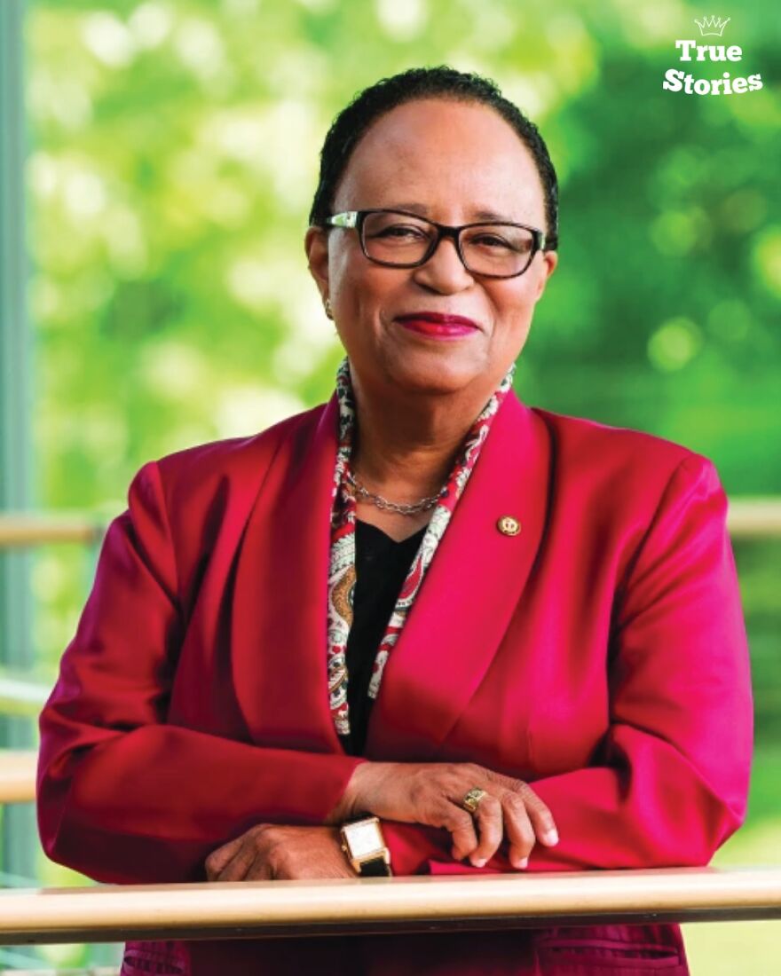 Portrait of an important American personality wearing glasses and a red blazer, smiling confidently in a natural setting.