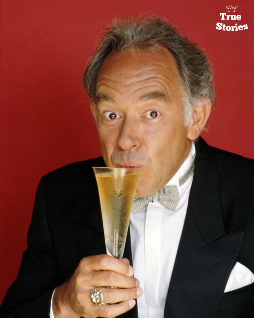 Middle-aged American personality in a tuxedo sipping champagne in front of a red background, portrait style.