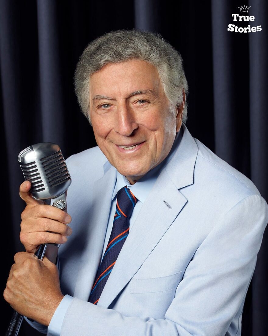 Older man in a light blue suit holding a vintage microphone, representing important American personalities in entertainment.