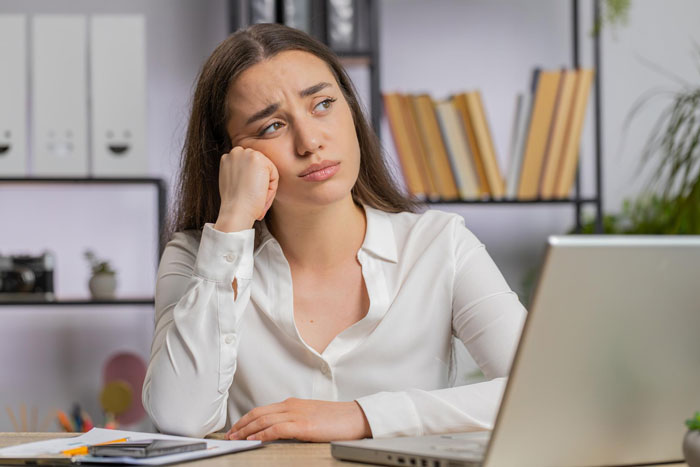 Young woman looking worried while working on a laptop, reflecting on challenges with an unemployed husband paying bills.