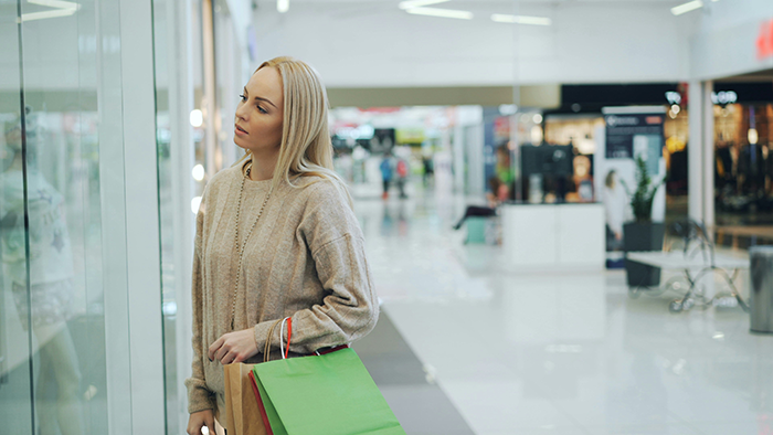 Woman shopping in mall looking thoughtful and holding bags, reflecting on SAHM financial challenges and fun money budget. Woman shopping in mall looking thoughtful and holding bags, reflecting on SAHM financial challenges and fun money budget.