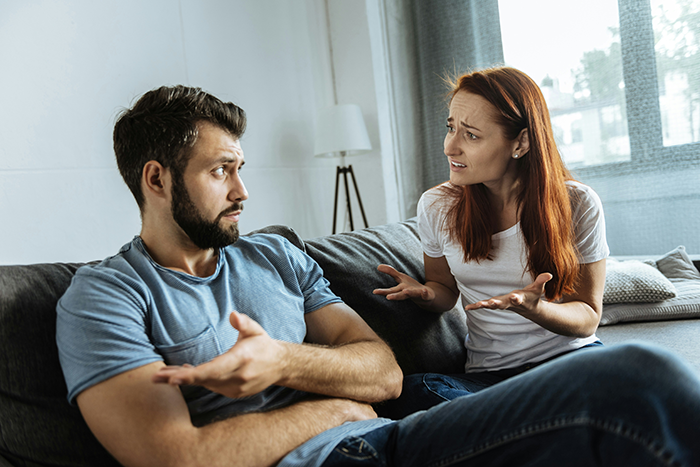 Couple having a tense conversation on a couch, illustrating a stay-at-home mom feeling poor despite receiving monthly fun money. Couple having a tense conversation on a couch, illustrating a stay-at-home mom feeling poor despite receiving monthly fun money.